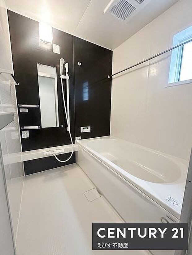 シンプルで清潔感のあるバスルームです。浴槽の形状が空間を有効に使いやすくなっています。窓があり換気しやすい設計です。落ち着いた配色の壁面が特徴的です。手すりやミラーも備わっています。