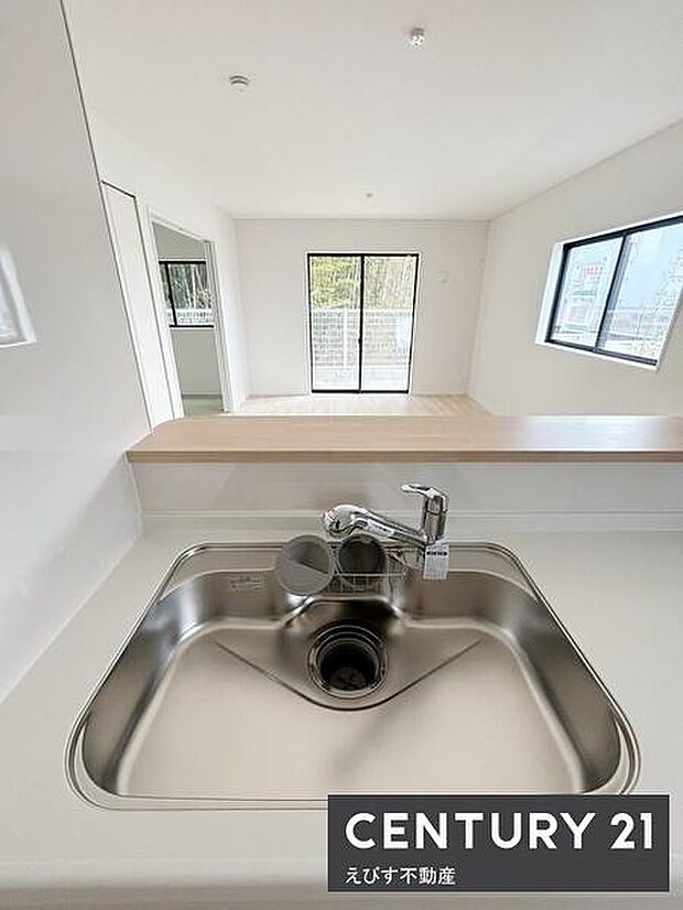 キッチンからリビングが見渡せる開放的なレイアウトです。大きな窓から明るい光が差し込む空間となっています。シンプルで手入れがしやすそうなシンクまわりも魅力です。すっきりとした印象のキッチンスペースです。