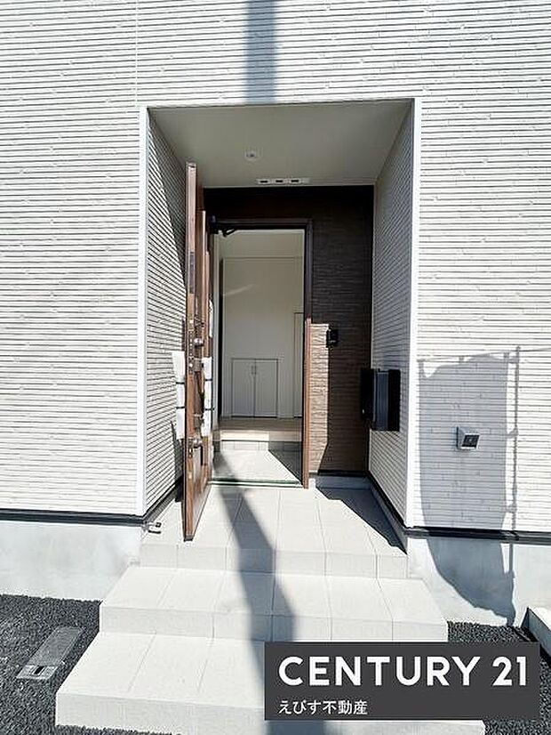 白を基調とした玄関で清潔感があります。段差のあるアプローチが落ち着いた雰囲気を演出しています。玄関ドアや壁面の直線的なデザインが印象的です。日差しが入るため明るく感じます。