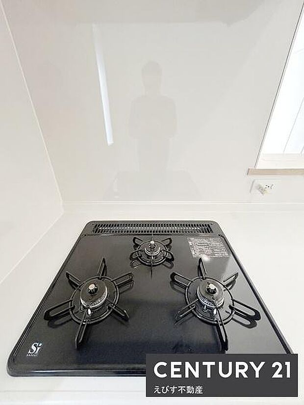 シンプルで清潔感のあるキッチンコンロが設置されています。お手入れしやすいフラットな天板が特徴です。ガスコンロは3口タイプで調理の幅が広がります。周囲もスッキリとした印象のキッチン空間です。
