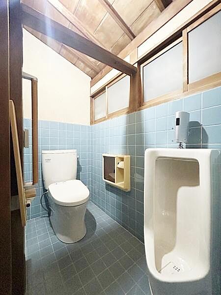 明るく開放的なトイレ空間になっています。タイル張りの壁と床が清潔感を演出します。窓付きで換気もしやすい設計です。洋式と小便器が備え付けられており実用性が高いです。