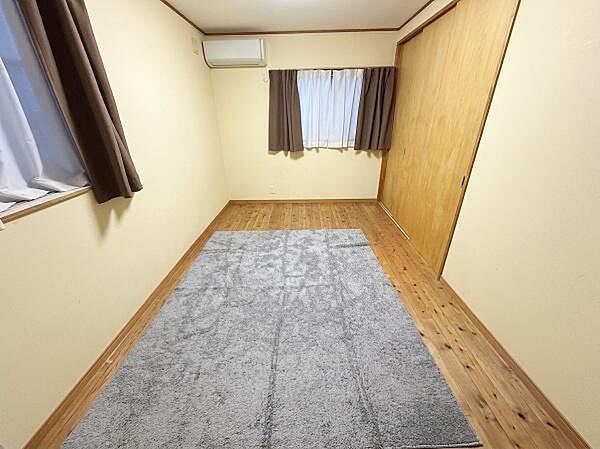 【一部AIによるモノ消し済み】シンプルなデザインで落ち着いた雰囲気の寝室です。窓が2つあり明るい日差しが差し込みます。床の木目が温かみを感じさせます。