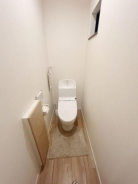 【一部AIによるモノ消し済み】シンプルなデザインのトイレ空間です。清潔感のあるホワイトの内装が印象的です。窓付きで明るさを確保しています。