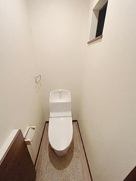 【一部AIによるモノ消し済み】シンプルなデザインのトイレです。小窓が設けられており明るさが感じられます。清潔感のある空間となっています。壁紙や床も落ち着いた色合いで統一されています。