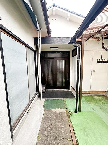 【一部AIによるモノ消し済み】玄関までのアプローチが屋根付きで天候を気にせず移動できます。落ち着いた色合いの玄関扉が印象的です。程よい広さのスペースで靴の脱ぎ履きもしやすそうです。