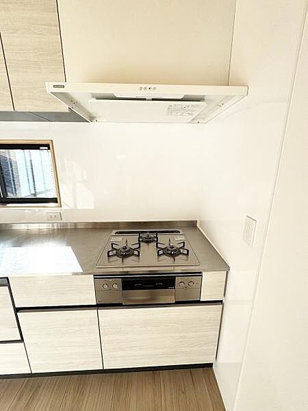 シンプルですっきりとしたキッチンが印象的です。コンロや収納スペースも機能的に配置されています。窓からの採光もあり明るい雰囲気です。使い勝手の良いレイアウトとなっています。清潔感を感じる内装です。