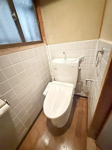 窓があるため換気がしやすいトイレです。壁には清潔感のあるタイルが使用されています。床は木目調で落ち着いた雰囲気があります。ウォシュレット機能付きで便利です。シンプルな空間が特徴です。