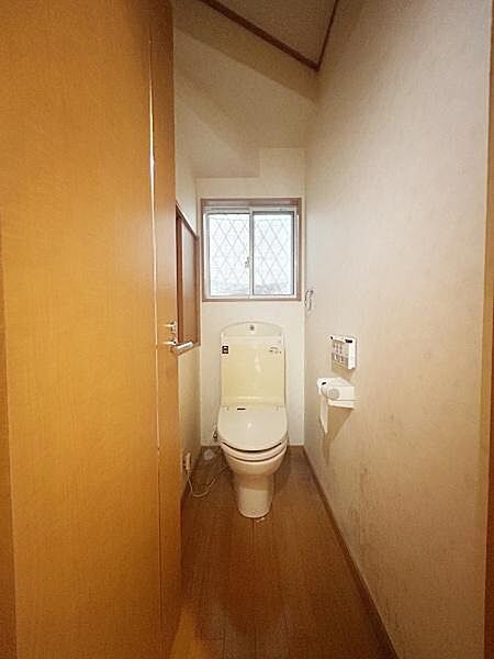 窓付きで明るい雰囲気のトイレです。落ち着いた木目調の床が印象的です。紙巻き器やリモコンも壁面に設置されています。シンプルなデザインで清潔感があります。換気もしやすい仕様です。