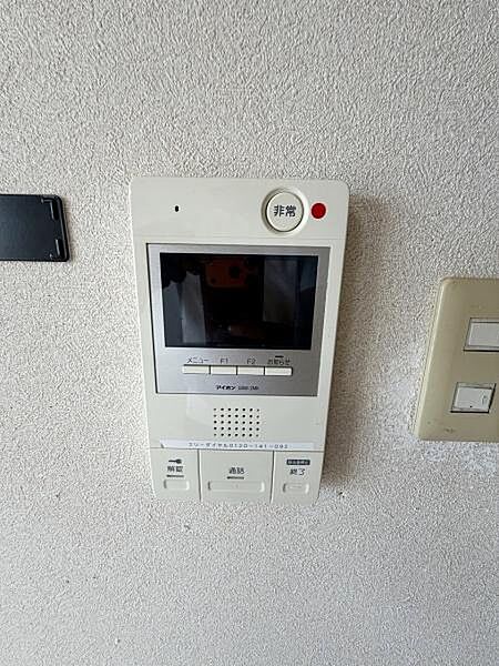 壁に設置されたモニター付きインターホンが確認できます。通話ボタンや非常ボタンが配置され来客の対応やセキュリティ面にも配慮されています。シンプルな操作パネルで使いやすいデザインです。