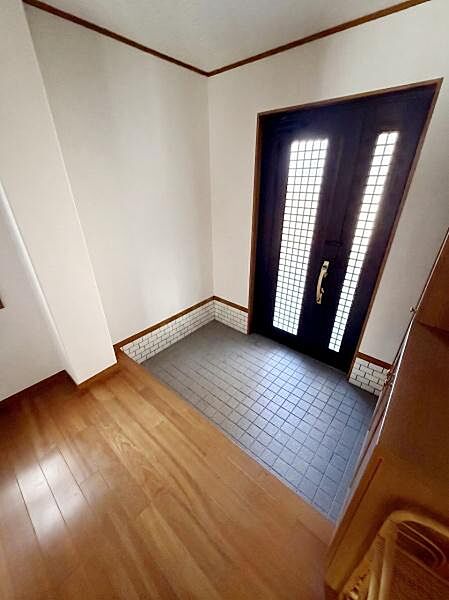 【一部AIモノ消し済み・実際の室内状況優先】玄関には松のフローリングを採用。明るい光が差し込む扉が開放感を演出します。タイル張りでお手入れもしやすい空間となっています。