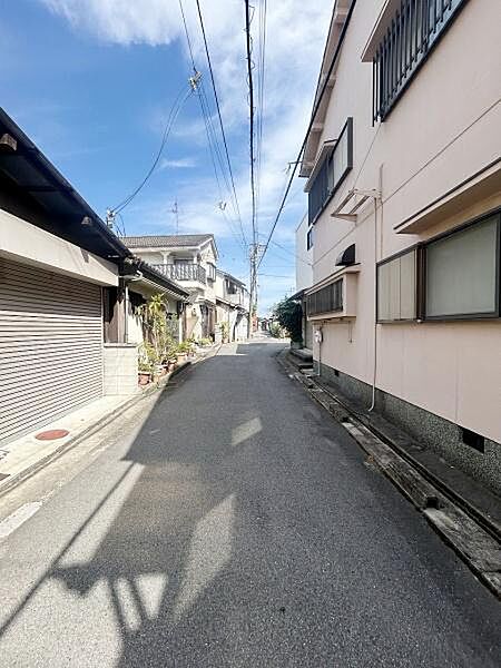 前面道路は舗装されており歩きやすい環境です。周囲には住宅が並び落ち着いた雰囲気が感じられます。空が広く日当たりも期待できる現地写真です。道路沿いの植栽や建物が整然としています。