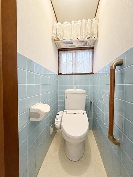 【一部AIモノ消し済み・実際の室内状況優先】水色のタイルで明るい雰囲気のトイレです。窓付きで自然光が入り換気もしやすい設計になっています。手すりが設置されており使い勝手に配慮されています。