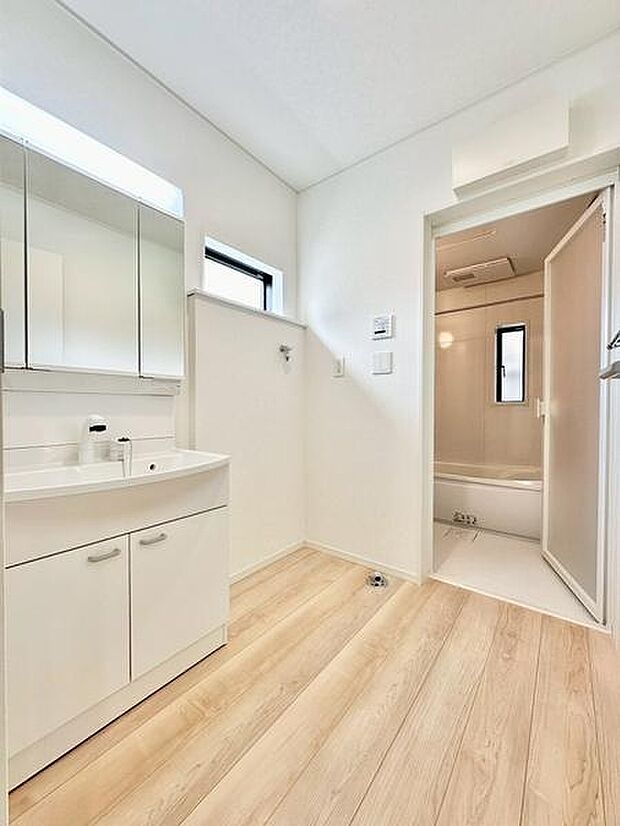 ナチュラルなフローリングと明るい壁で開放感のある洗面台・洗面所です。三面鏡で日々の身だしなみも快適に。窓があり自然光が差し込みます。浴室とのアクセスも便利な設計です。