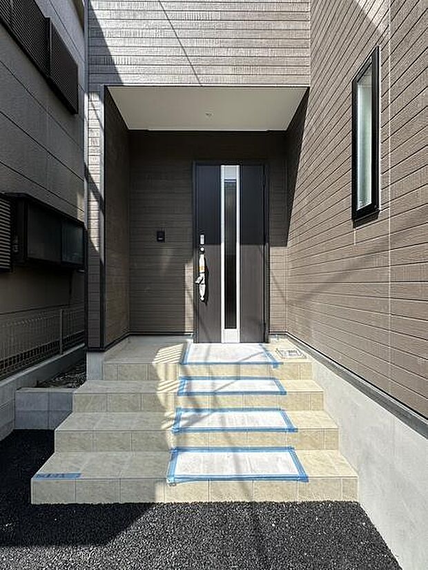 明るい色合いの階段がエントランスに落ち着いた印象を与えます。玄関ドアのデザインがシンプルでスタイリッシュです。外壁の配色が統一感を演出しています。採光窓が玄関まわりに開放感をプラスしています。