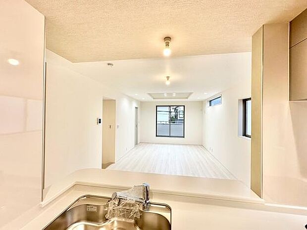 （LDK18帖）明るい色合いの床材が開放的な雰囲気を演出しています。複数の窓から自然光が差し込むリビングです。天井のダウンライトが室内を均一に照らします。