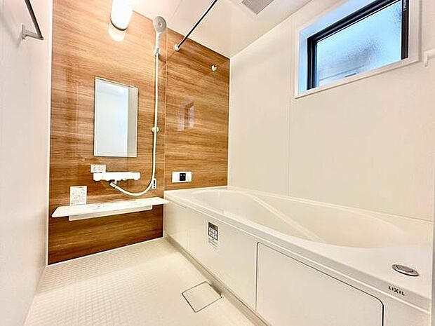 明るい光が差し込むバスルームです。木目調のアクセントパネルが落ち着いた雰囲気を演出します。浴槽が広くゆったりとしたスペースが確保されています。滑りにくい床材が採用されており安全面にも配慮されています。