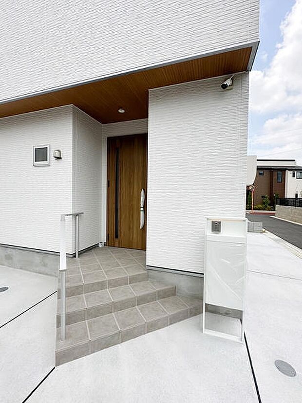 シンプルなデザインの玄関が印象的です。タイル張りのアプローチは清潔感があります。手すりも設置されていて安心してご利用いただけます。宅配ボックスも備えられており利便性が感じられます。