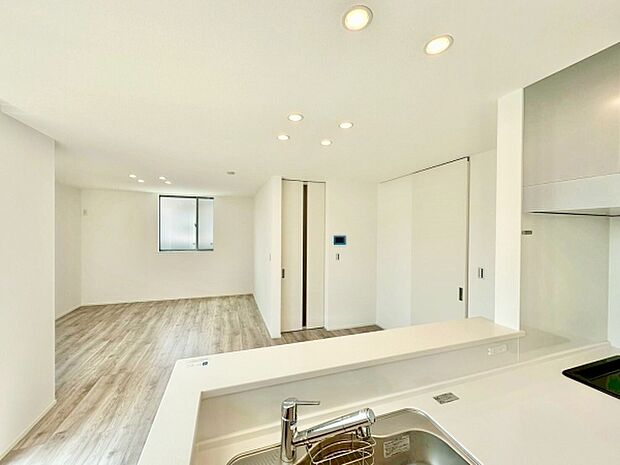 シンプルで洗練されたリビングはすっきりとした印象を与えます。フローリングが明るく開放感を演出しています。埋め込み照明が落ち着いた雰囲気をつくり出しています。キッチンからリビングが見渡せる設計です。