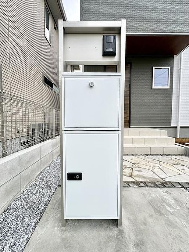 玄関前にはシンプルなデザインのポストが設置されています。アプローチの石畳が落ち着いた印象を与えます。玄関扉までの動線もスムーズです。建物外観と調和した色合いが際立っています。