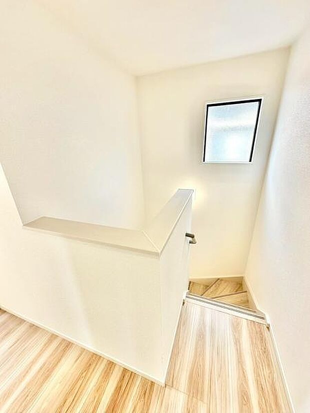 階段上部の壁に設けられた窓から光が差し込み空間全体が明るく感じられます。手すり付きで安心して階段の昇降ができます。床の木目調が清潔感を与えています。余計な装飾がなくすっきりとした印象です。
