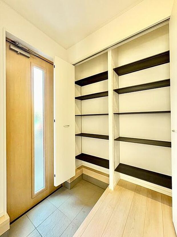 明るい玄関スペースには収納棚が充実しており整理整頓しやすい設計です。木目調の扉が温かみを演出しています。シューズや小物をきちんと収納できる点が特徴です。床の段差もアクセントになっています。