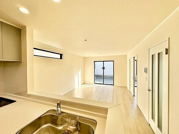 【16帖LDK】大きな窓から自然光がたっぷり入る明るいリビングです。白を基調にした内装が開放感を引き立てます。カウンターキッチンから全体を見渡すことができます。