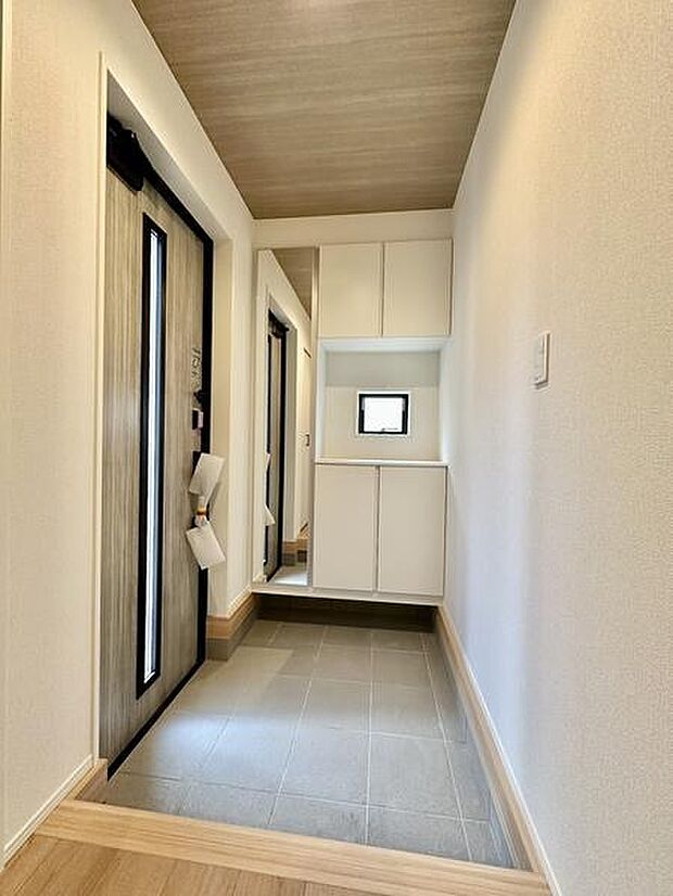 すっきりとした玄関スペースで収納もたっぷり備え付けられています。明るい木目調の天井と自然光が広がる空間を演出しています。シンプルなデザインで清潔感が感じられます。玄関全体がスマートにまとまっています。