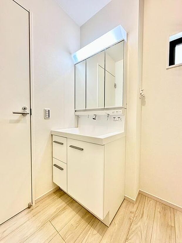 洗面台は直線的なデザインが特徴で明るい照明がしっかりと手元を照らします。収納スペースも豊富で整理がしやすい仕様です。ナチュラルなフローリングとの調和が感じられる空間です。