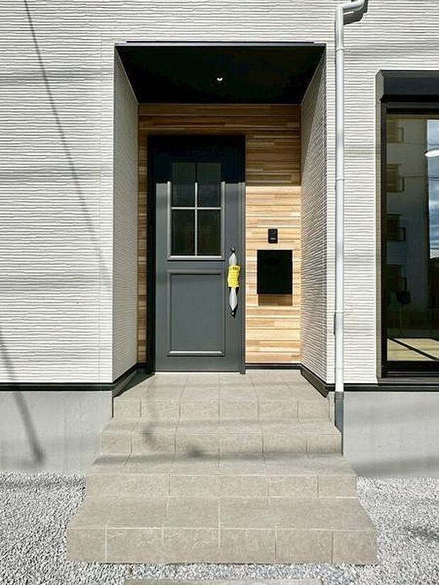 シンプルで落ち着いた色合いの玄関扉が住まいの雰囲気を引き立てます。木目調のアクセントウォールが温もりを演出しています。窓からの採光も期待できる明るい玄関まわりです。