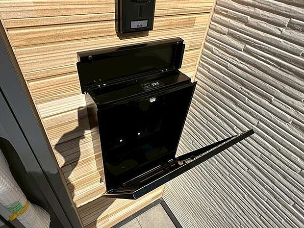 スタイリッシュな外観に調和する黒色のポストが設置されています。壁面のデザインが印象的で建物の印象を引き立てます。前面道路からも目につきやすい位置に設置されています。