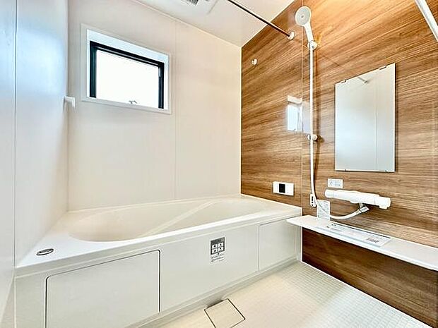 清潔感のある明るいバスルームです。木目調の壁面が空間に落ち着きを与えています。大きな窓から自然光が差し込み換気も良好です。収納スペースも確保されており使いやすい設計です。