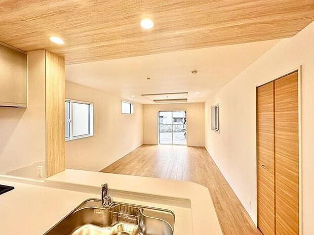 木目調の天井とフローリングが空間全体に統一感を与えています。大きな窓から自然光が差し込み開放感を感じられます。ダウンライトの照明が室内を均一に明るく照らしています。