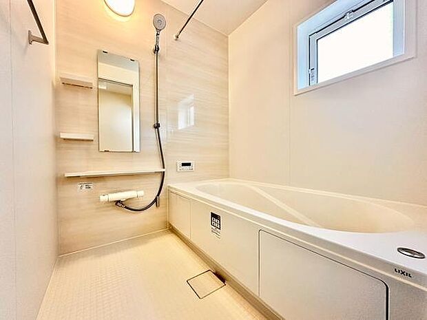 明るい色調の壁と大きな浴槽が印象的なバスルームです。窓から自然光が入り換気もしやすい造りになっています。手すりや棚も設置されており機能面も充実しています。シャワーと鏡の配置もバランスが良いです。