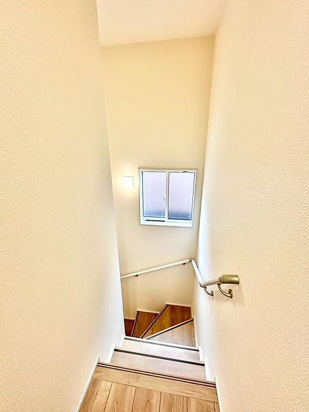 手すりが設置されているため安全に昇り降りできる階段です。窓から自然光が入り明るい空間が広がります。シンプルなデザインで清潔感があります。木目調の床材がアクセントとなっています。