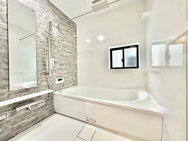 浴室は明るい色調とアクセントクロスが特徴的で清潔感のある空間です。大きな鏡と広々とした浴槽が設置されています。窓付きで換気に配慮されています。バスルーム全体がすっきりとした印象です。