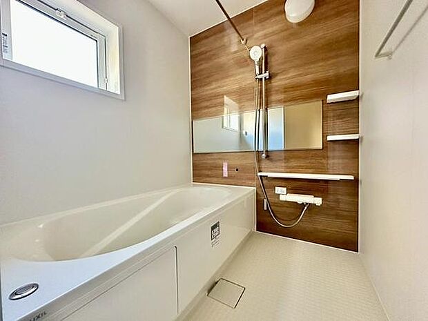 木目調パネルがアクセントになり洗練された印象のバスルームです。大きな鏡と収納棚が備わり使い勝手も考えられています。明るい窓から自然光が入り清潔感のある空間になっています。