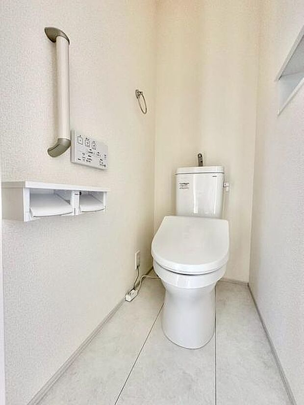 明るい色合いの内装で清潔感のあるトイレです。手すりが設置されており使いやすさにも配慮されています。ペーパーホルダーとリモコン操作パネルがすっきりとまとまっています。床の色合いが空間を広く見せています。