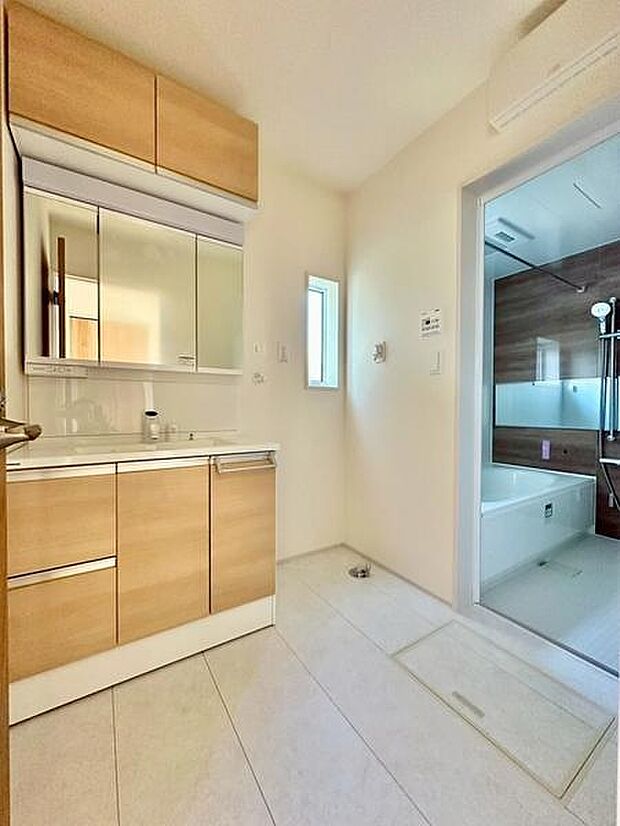 木目調の洗面台がやわらかな雰囲気を演出しています。収納スペースも豊富ですっきりと整理できます。明るい空間で毎日の利用が快適です。バスルームへの動線もスムーズです。窓があり自然光が差し込む洗面所です。