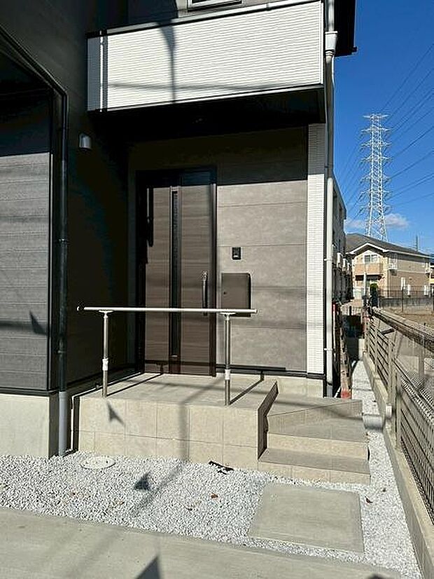 モダンなデザインの玄関が印象的です。手すりが設置されており段差も配慮されています。直線的なアプローチでエントランスまでの動線も確保されています。玄関前のスペースにも余裕があります。