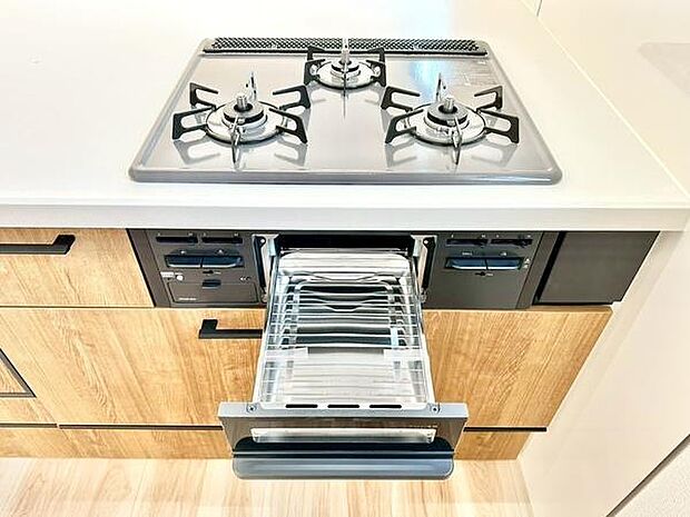 ガスコンロとグリルが一体となったキッチンです。作業スペースもゆとりが感じられます。木目調の扉が空間になじみすっきりとした印象を与えます。収納も多く整理しやすい仕様です。