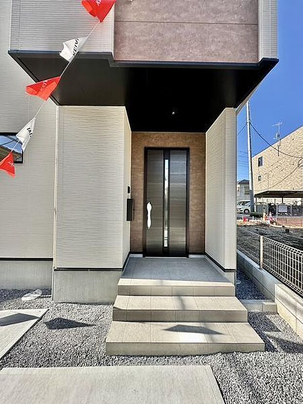 モダンなデザインの玄関が印象的です。ゆったりとしたアプローチがあり玄関への段差が少なく安心です。落ち着いた色合いが建物全体に調和しています。雨除けの庇もあり実用的な仕上がりです。