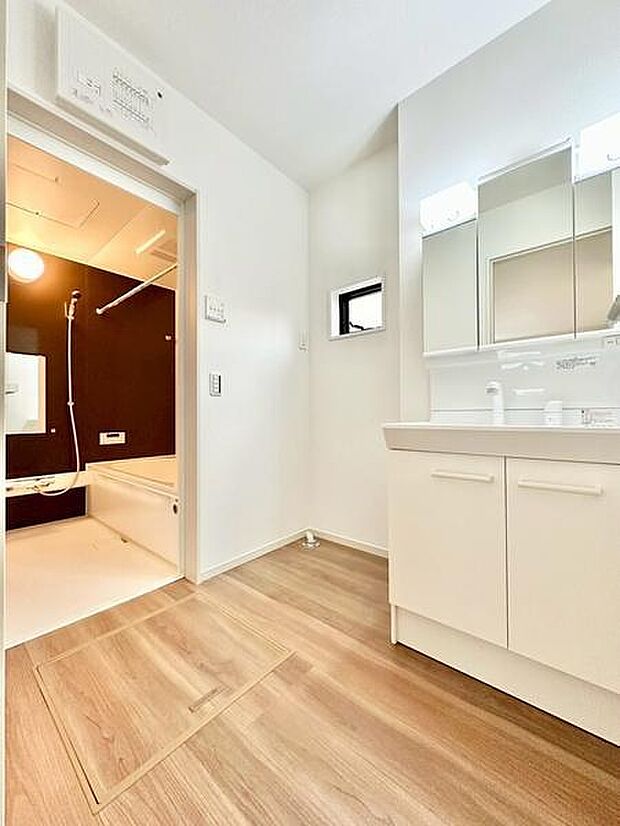 ナチュラルな木目調の床が清潔感を引き立てる洗面所です。明るい照明と大きなミラーが空間を広く感じさせます。浴室との動線も良好で使い勝手に配慮されています。