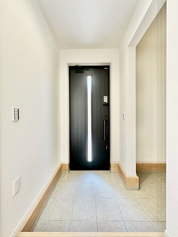 白を基調とした明るい玄関スペースです。スタイリッシュな扉が空間を引き締めています。段差に配慮された設計が特徴です。床はシンプルで清潔感があります。玄関から室内へスムーズに移動できます。