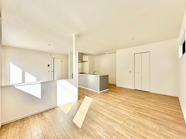 【20.9帖LDK】明るい陽射しが差し込むリビングは空間が広く感じられます。ナチュラルなフローリングが柔らかな印象を演出しています。白を基調とした壁が開放的な雰囲気を引き立てています。