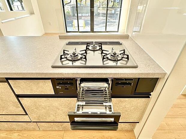 窓からの光が差し込むキッチンは明るく開放感があります。3口ガスコンロとグリルが備わっており調理がしやすい仕様です。足元の収納も充実しており整理整頓に便利です。使い勝手の良いレイアウトが魅力です。