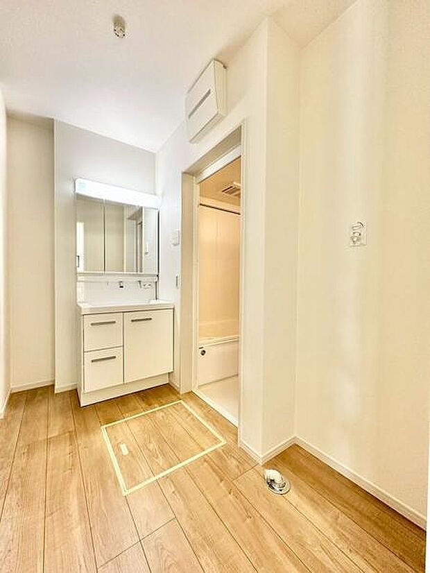 洗面台と浴室が隣接しており毎日の身支度に便利なレイアウトです。明るい室内が清潔感を演出しています。木目調の床が温かみを感じさせます。収納スペースも備えておりすっきりとした空間です。