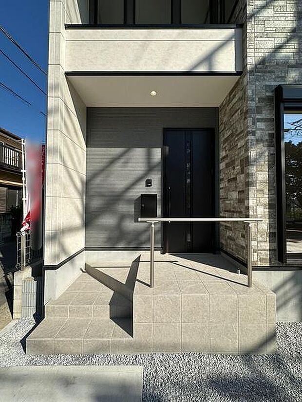 シンプルで落ち着いた玄関スペースです。モダンなタイルデザインが特徴的です。手すりがあり安心してご利用いただけます。玄関ドアの存在感が際立っています。建物外観と調和のとれた仕上がりです。