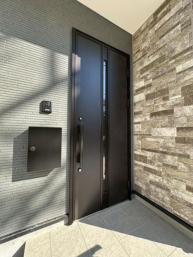 モダンなデザインの玄関ドアが印象的なエントランス空間です。外壁の異なる素材感が調和し洗練された雰囲気を演出しています。ポストやインターホンもすっきりと配置され使い勝手にも配慮されています。