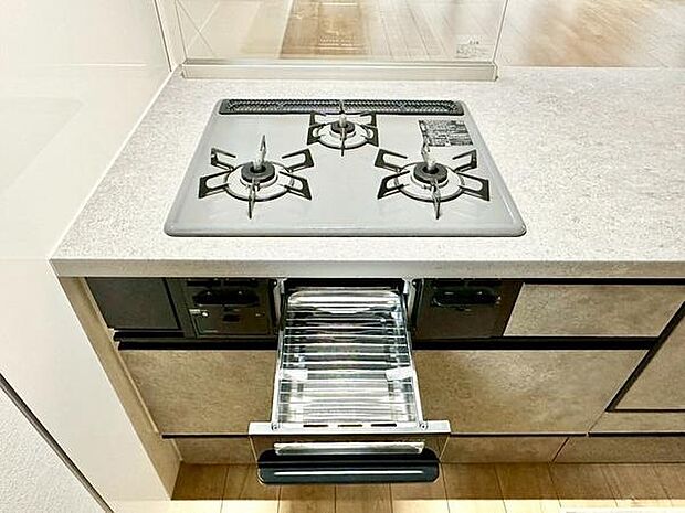 シンプルなデザインのキッチンで全体がすっきりとまとまっています。三口コンロが設置されており料理の効率も向上します。魚焼きグリルも備え付けられているため調理の幅が広がります。