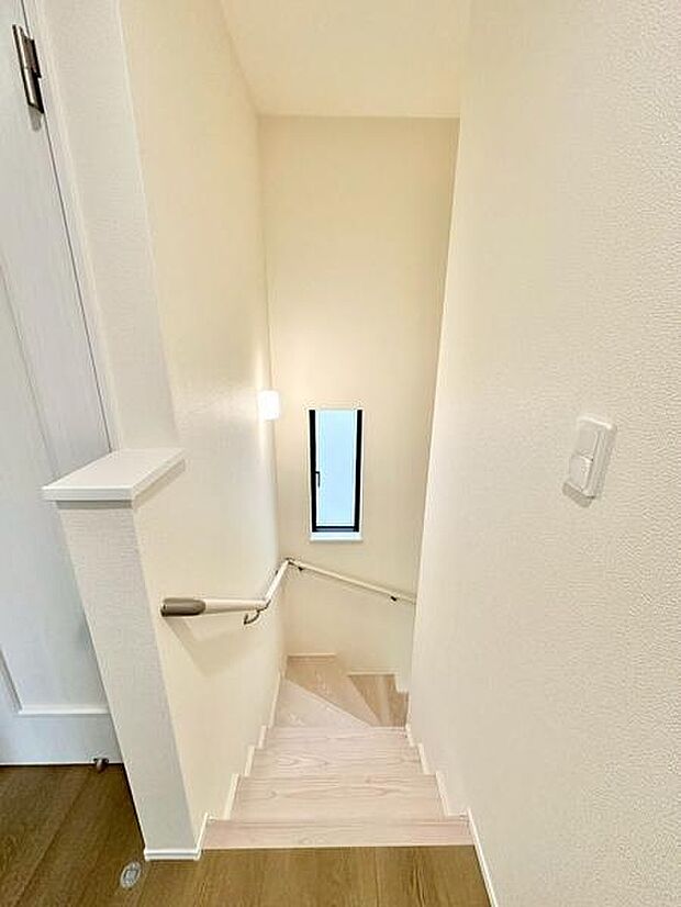 階段には手すりが設置されており安心して上り下りできます。明るい壁面と小窓からの光が階段スペースを爽やかに演出します。清潔感のある空間で日常の動線も快適です。シンプルなデザインが特徴的です。